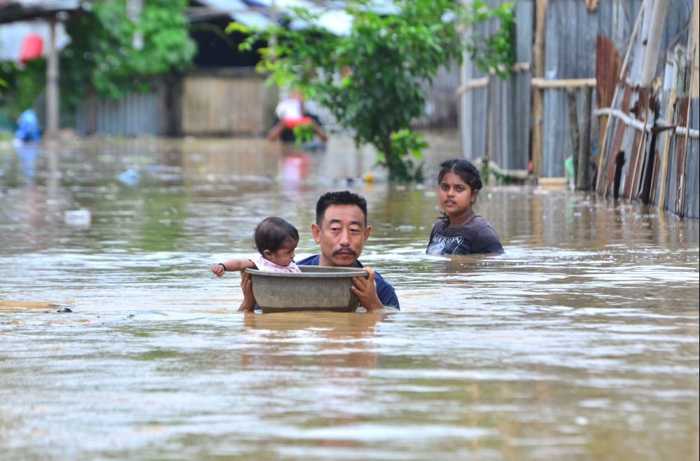 A man helps a toddler in a basket move to higher ground in a flooded area at Vilhume Colony after a heavy rainfall in Dimapur on June 11. (Photo by Caisii Mao)